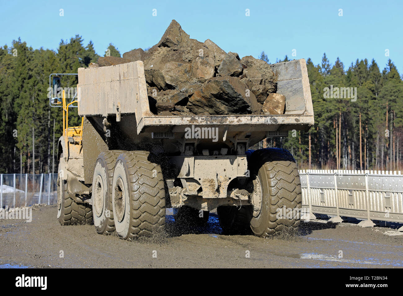 Articulated dumper with load of stone and gravel at work on a muddy construction site on a day of spring, rear view. Stock Photo