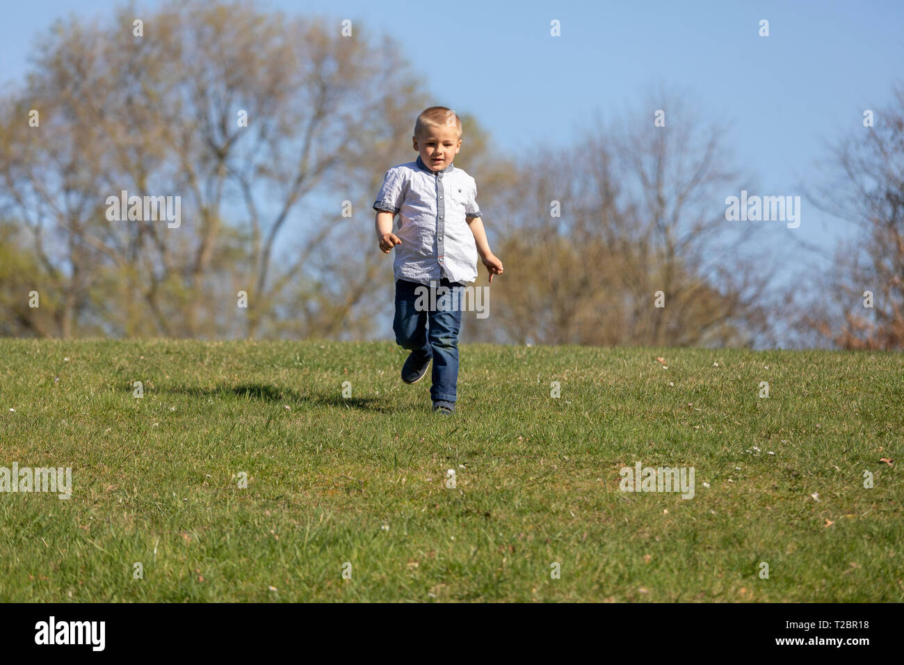 Cute boy running across grass und smiling Stock Photo - Alamy