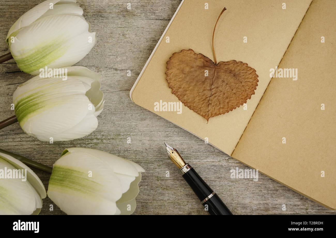 Fountain pen and kraft notebook on wooden surface., with white flowers