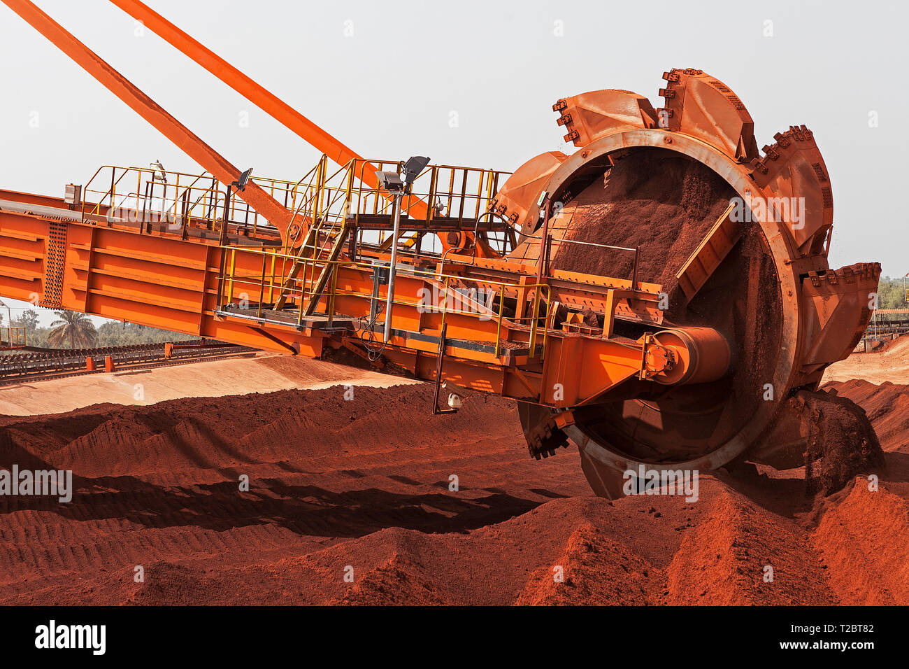Port operations for managing and transporting iron ore. Bucket wheel of reclaimmer stacker using buckets to stack ore from stock on conveyor to ship Stock Photo
