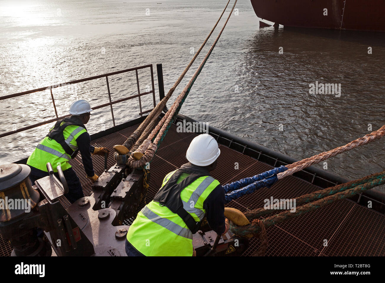 Port operations for managing and transporting iron ore. Dolphin jetty mooring facility with riggers using quick release rope hooks as ship sets sail Stock Photo