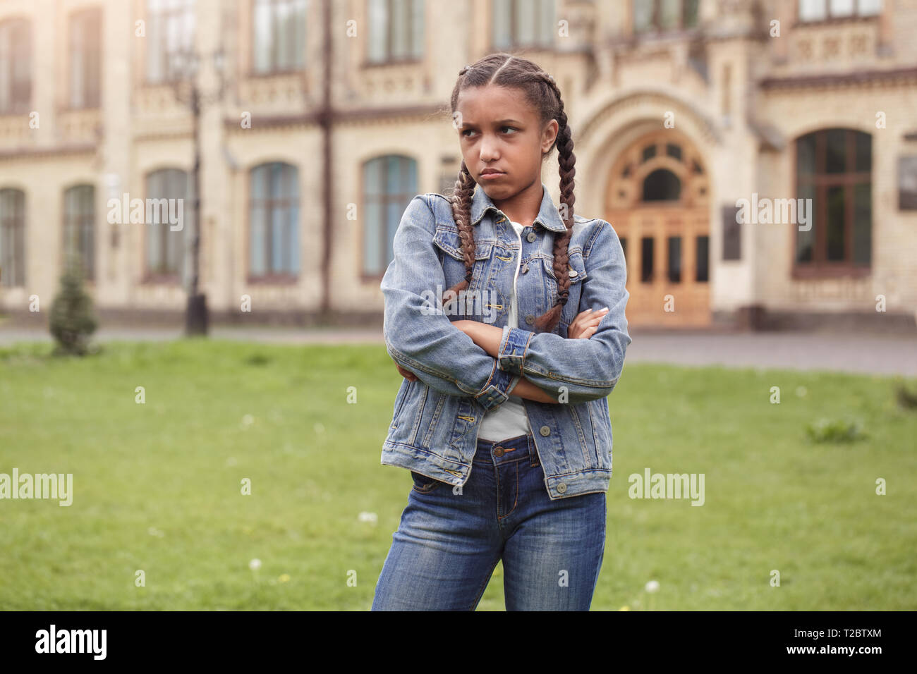 Young african american girl wearing jeans jacket standing at school yard  crossed arms looking aside capricious Stock Photo - Alamy