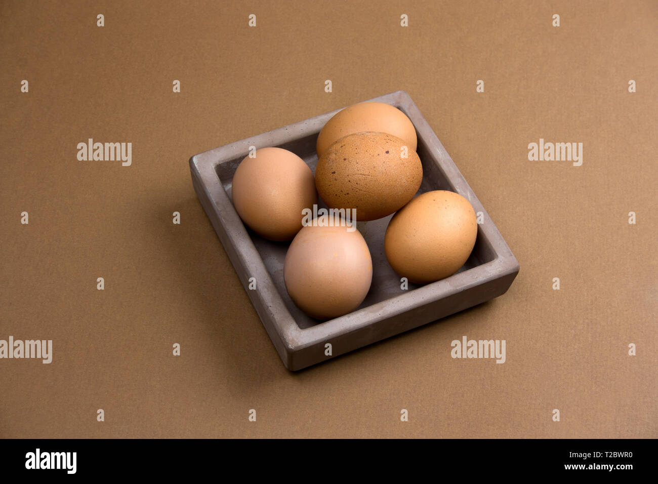 brown eggs in ceramic square plate on brown background Stock Photo