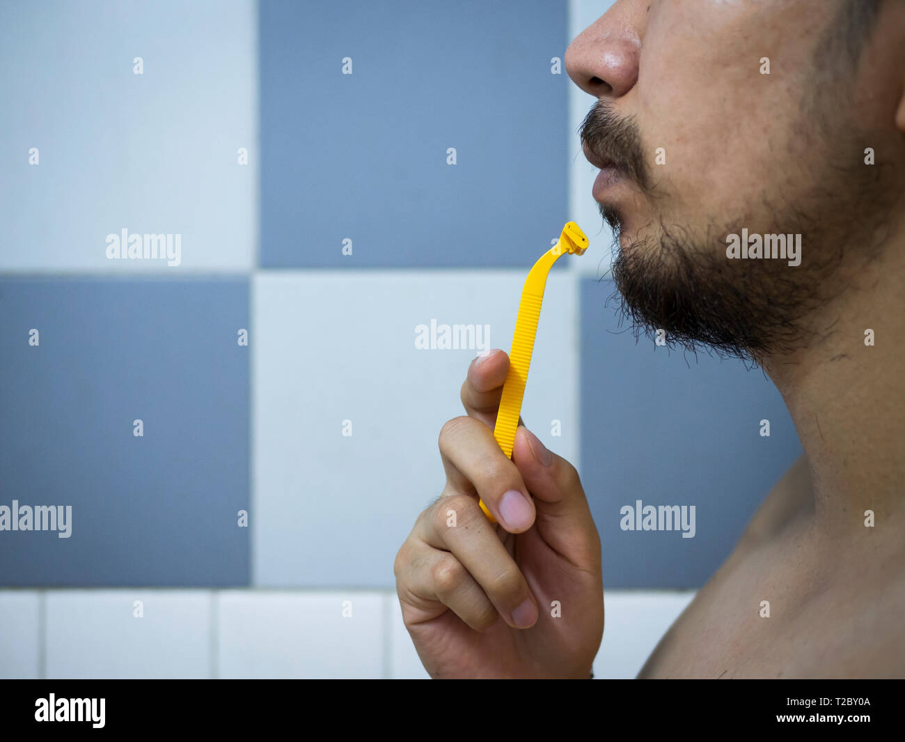 closeup man use yellow shaver shaving messy beard and mustache on his face in bathroom Stock Photo