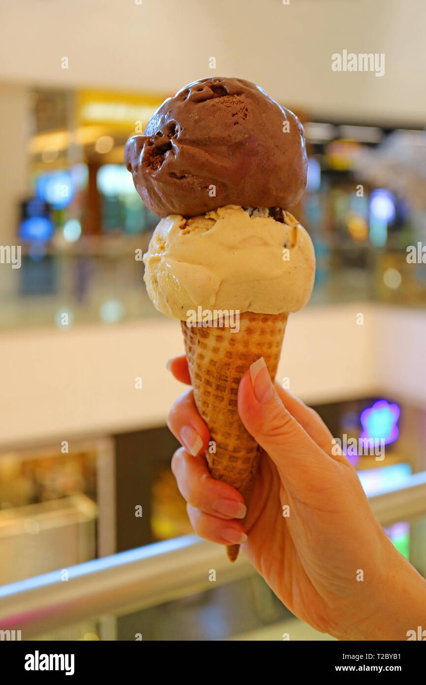 Vertical image of hand holding ice cream cone with two scoops of chocolate and peanut butter ice Stock Photo