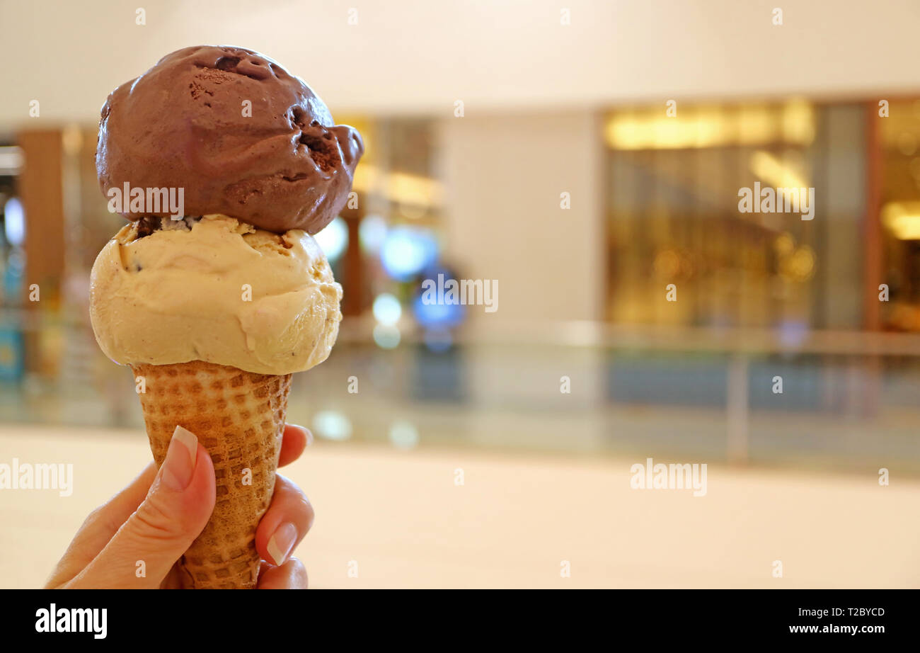 Woman's hand holding ice cream cone with two scoops of chocolate and peanut butter ice Stock Photo