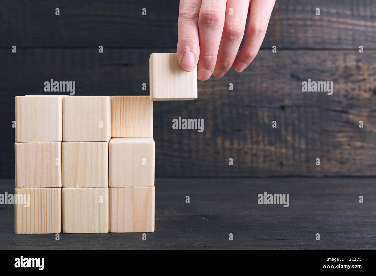 Woman's hand putting the final piece of wooden cube into place - achievement concept. Finish the project concept Stock Photo