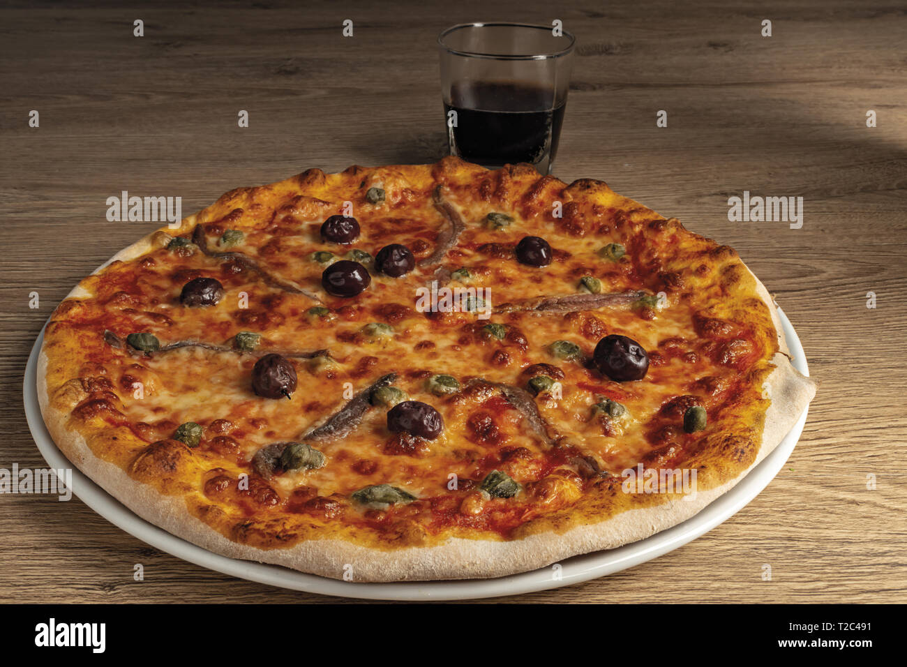 pizza pomodoro acciughe capperi olive nere intera nel piatto Stock Photo