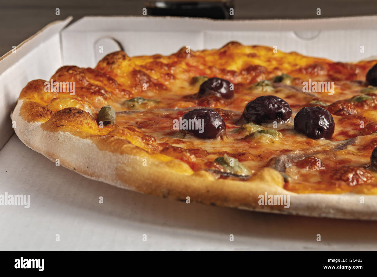 pizza pomodoro acciughe capperi olive nere intera nella scatola dal basso primo piano vista sinistra Stock Photo