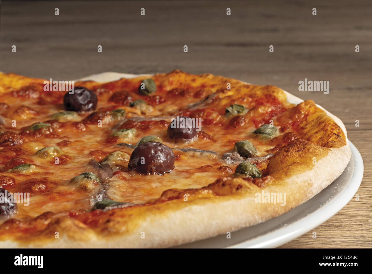 pizza pomodoro acciughe capperi olive nere intera nel piatto da basso primo piano vista destra Stock Photo