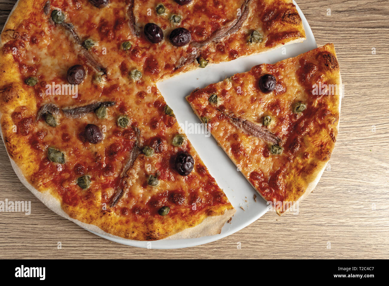 pizza pomodoro acciughe capperi olive nere tagliata nel piatto dal basso primo piano vista destra Stock Photo