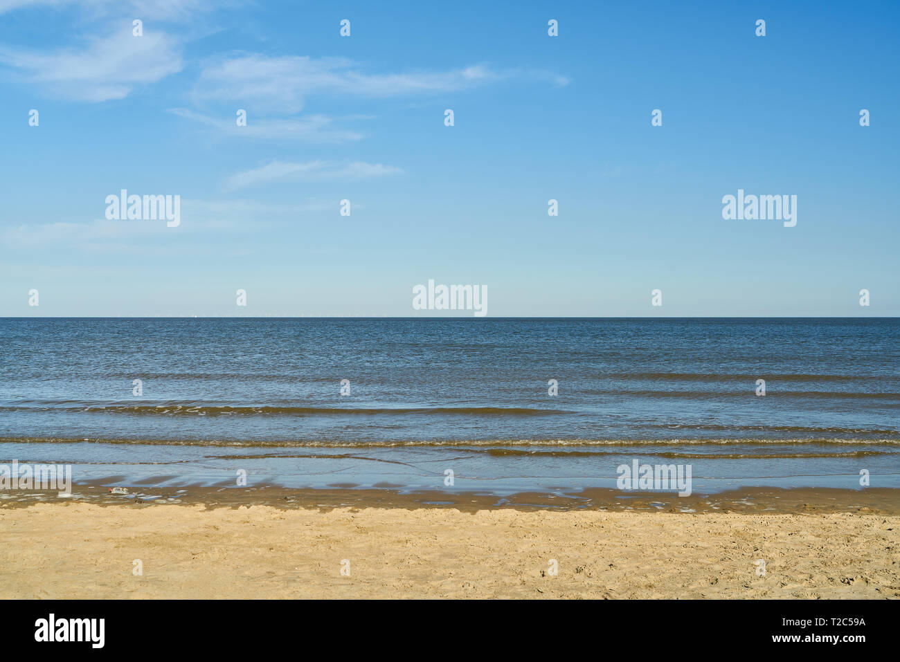 Small waves in the sea on the beach in front of a blue sky with clouds ...
