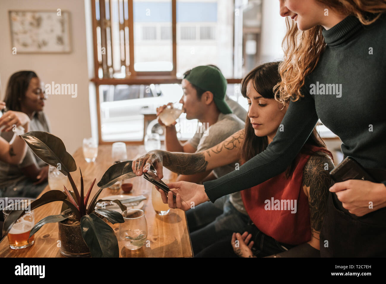 Customer using her cellphone and an nfc terminal to pay for the check in restaurant while out with friends Stock Photo