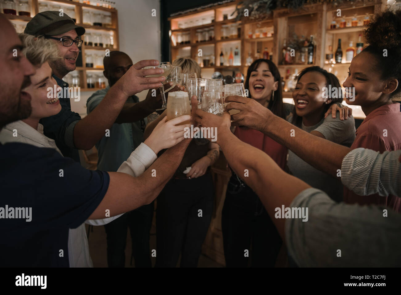 Diverse group of young friends cheering with drinks while hanging out together in a bar in the evening Stock Photo