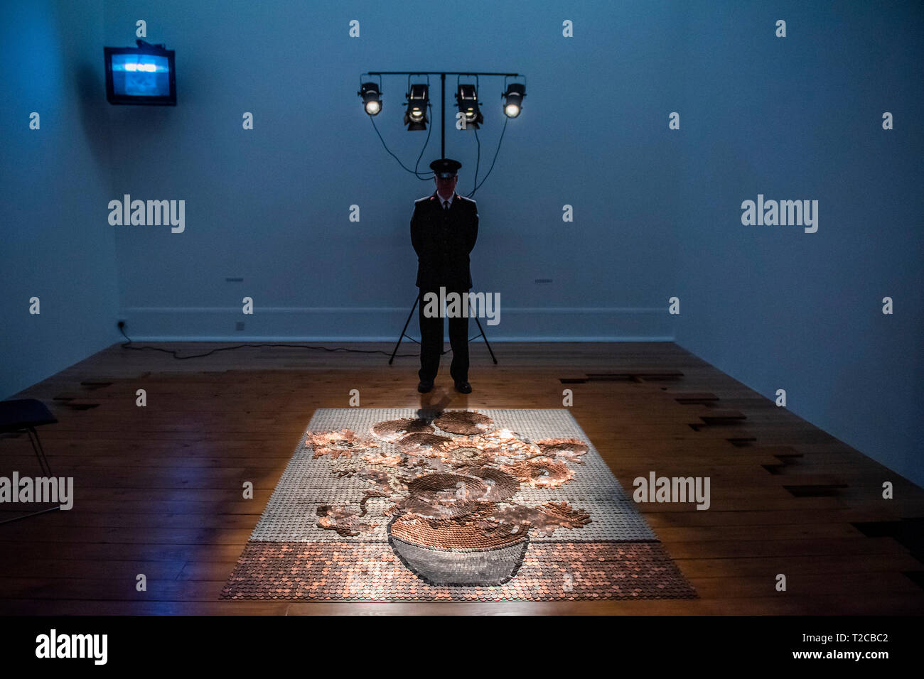 London, UK. 01st Apr, 2019. Rose Finn-Kelcey’s Bureau de Change 1987 coincides with The EY Exhibition: Van Gogh and Britain (27 March – 11 August 2019). The live installation consists of £1,000 worth of coins laid out on the floor in the image of Vincent van Gogh’s iconic Sunflowers, overseen throughout each day both by an actor appearing as a guard in period uniform and a CCTV camera that films the coin-picture, transmitting the image to a monitor in the space. Credit: Guy Bell/Alamy Live News Stock Photo