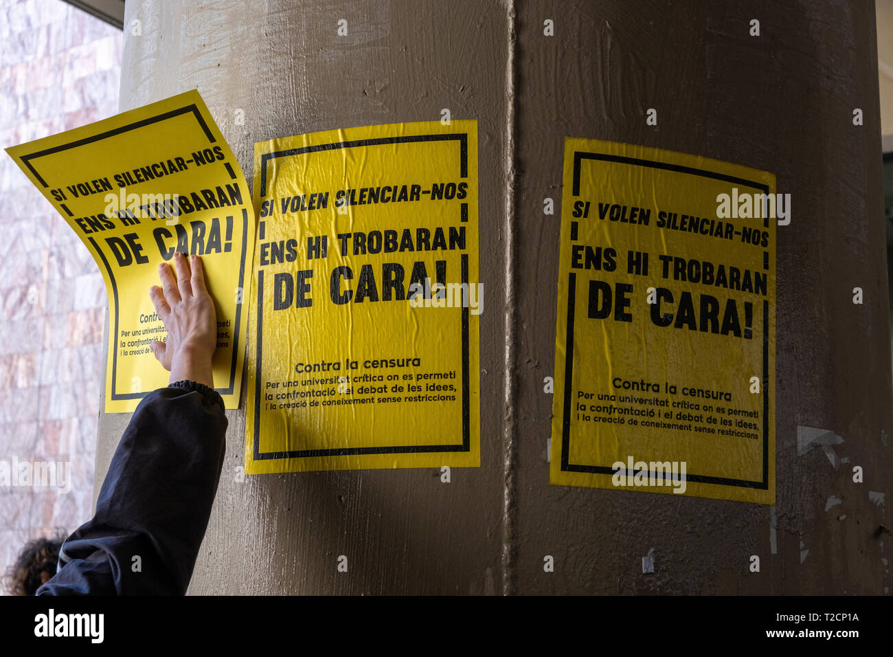 A hand is seen placing placards  against censorship during the protest on to a wall. As a result of the Central Electoral Board order to withdraw public space of all kinds of symbols related to the Catalan independence movement during the election period, the Union of students of the Catalan countries have hanged placards at the university campus of the UB- Raval to condemn the censure of such decision. Stock Photo