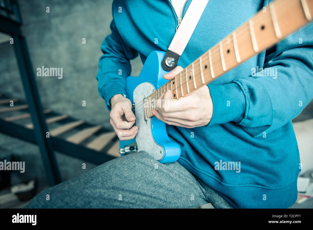 Professional musician in bright sweatshirt carrying blue electronic guitar Stock Photo