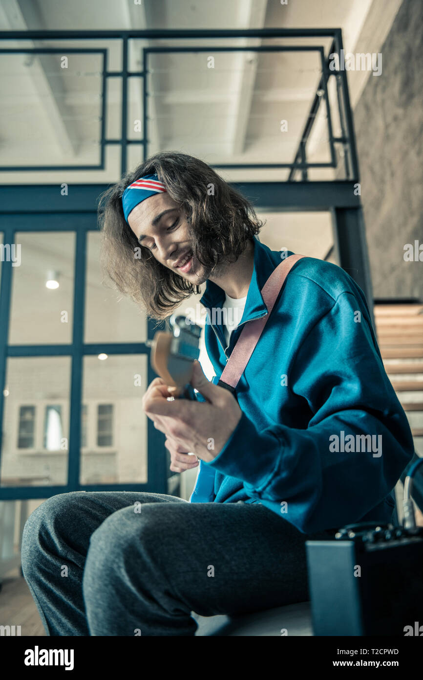 Contented dark-haired inspired man in blue sweatshirt carrying guitar Stock Photo