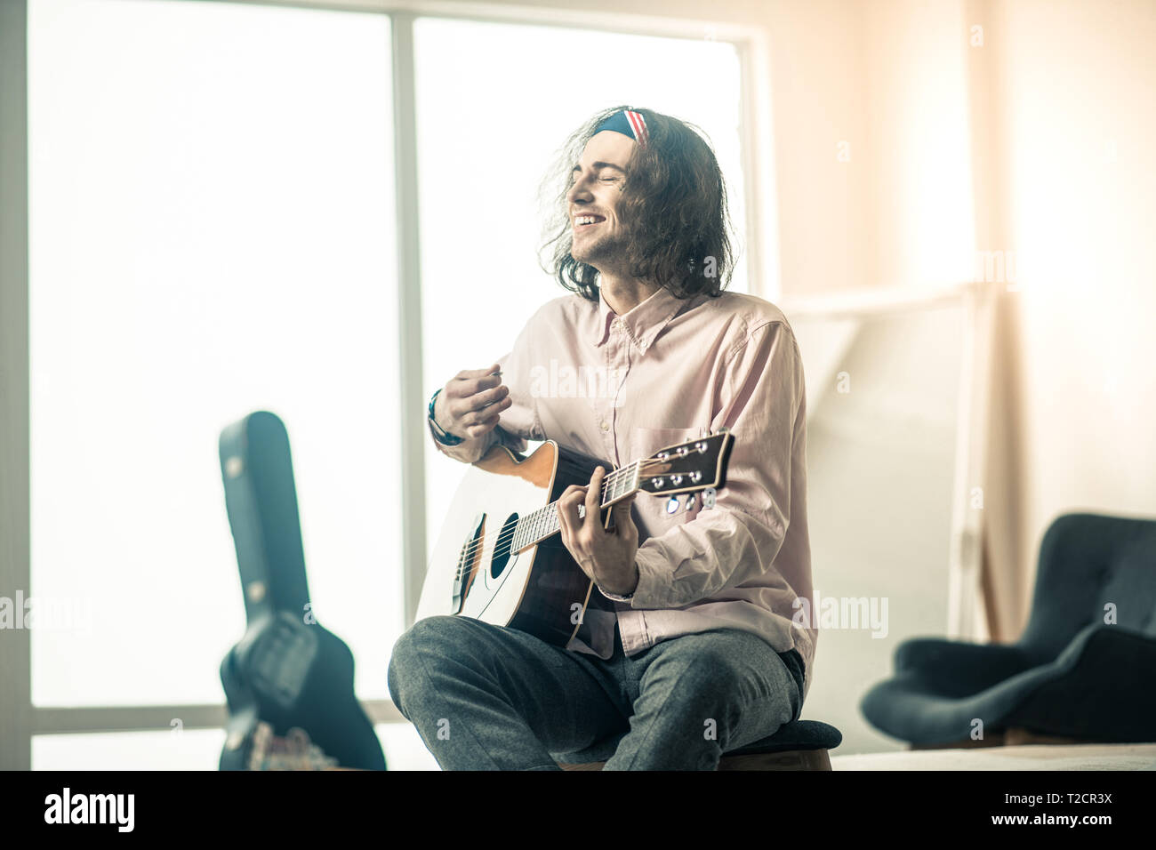 Cheerful handsome young guitarist sitting in bright room Stock Photo