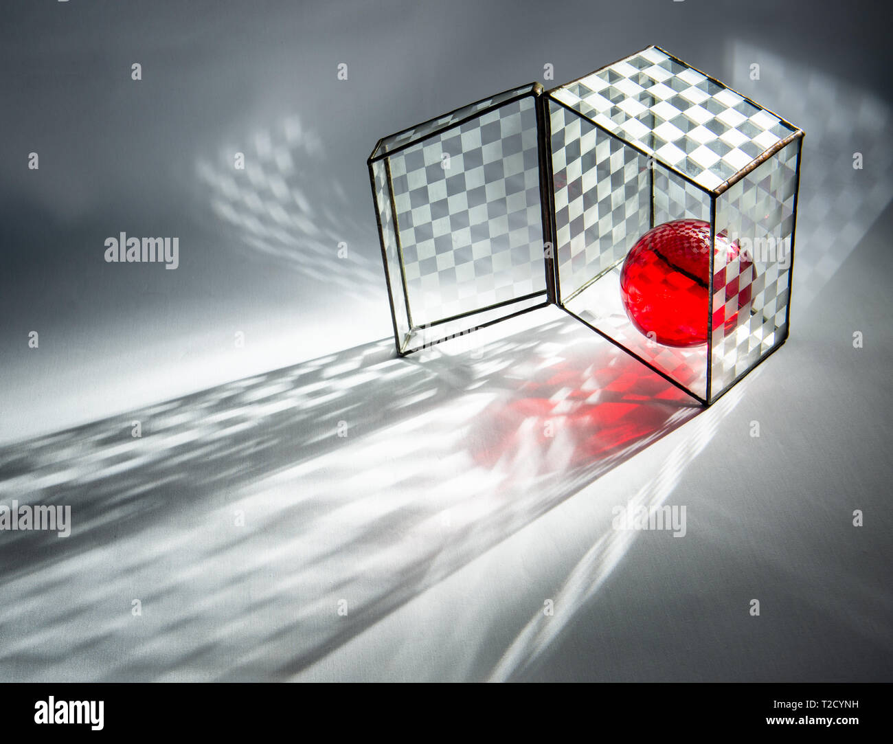 Red glass ball inside checkered glass box. Stock Photo