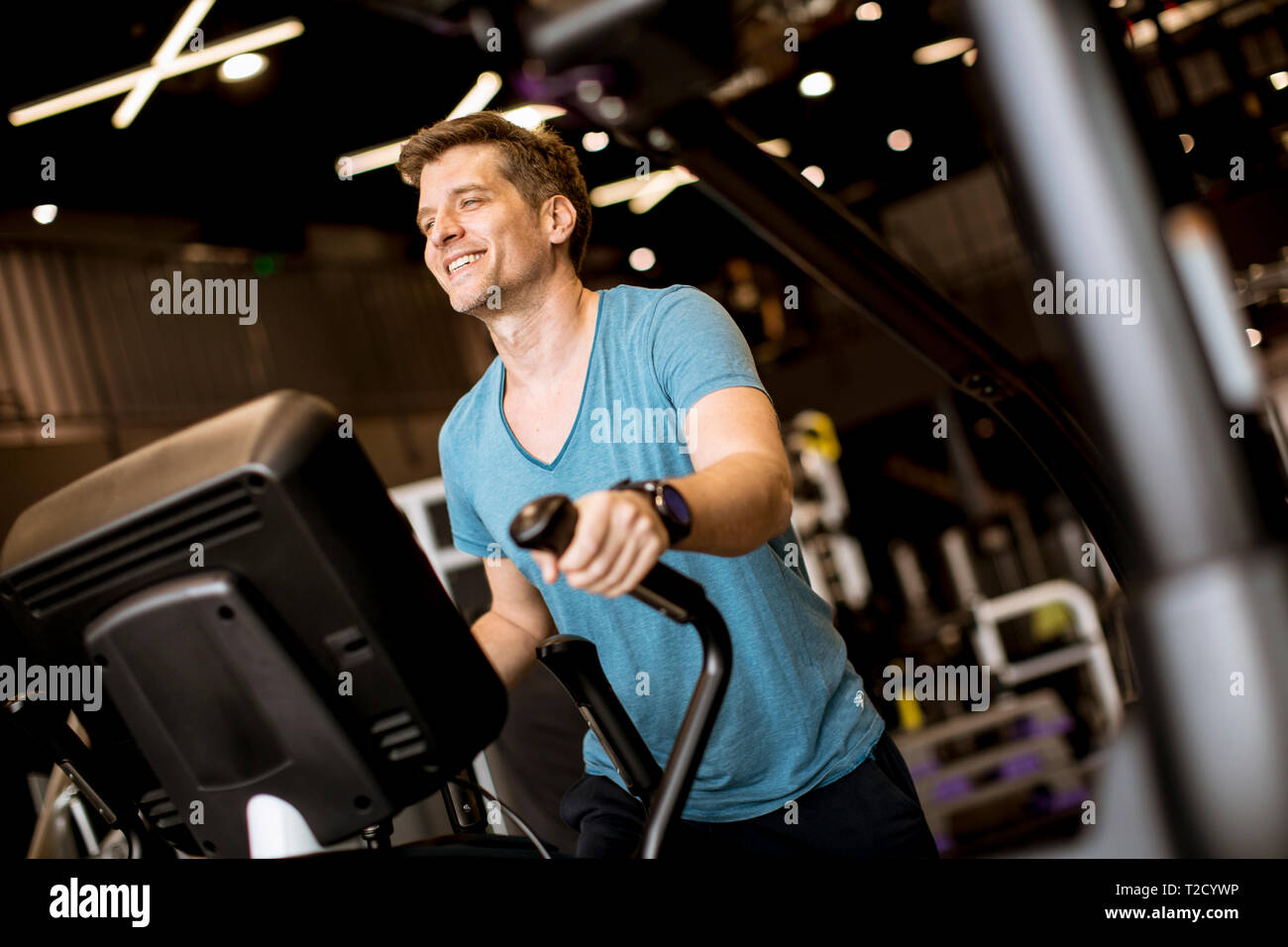 Young man doing exercise on elliptical cross trainer in sport fitness gym club Stock Photo