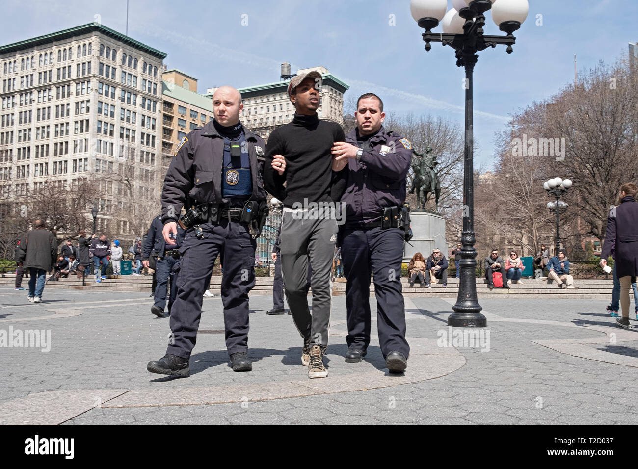 Two policemen arresting a young African American male and leading him away in handcuffs. At Union Square Park in Lower Manhattan, New York City Stock Photo