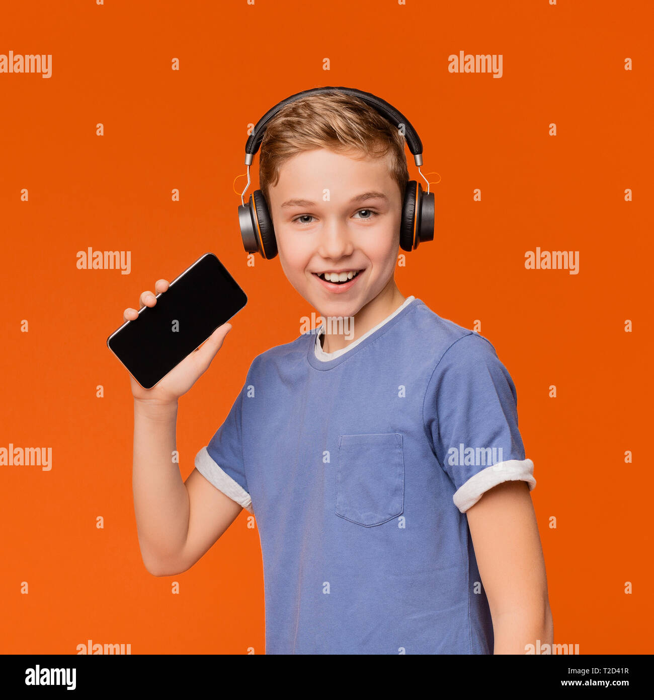 Cute smiling boy singing into smartphone like microphone and listening ...