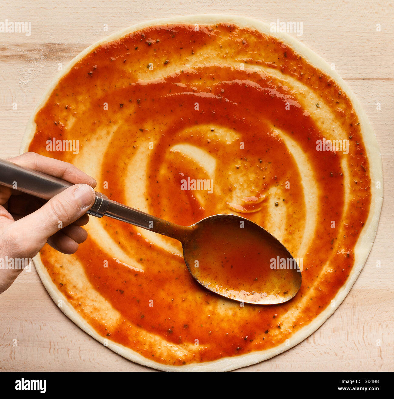 Chef adding sauce, spreading tomato paste on pizza base, top view, crop