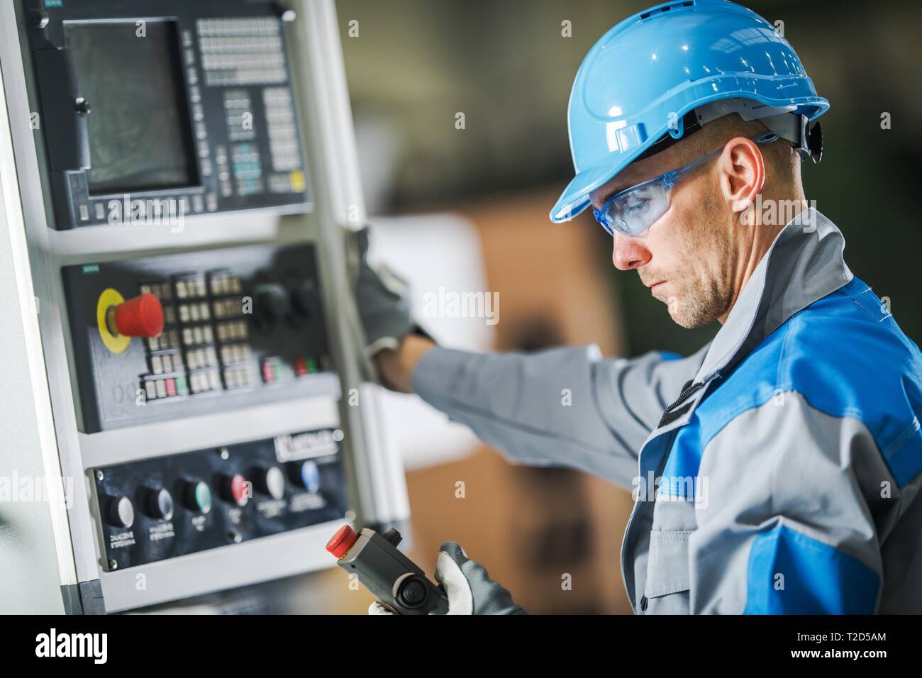 Caucasian CNC Machine Operator Wearing Blue Hard Hat and Safety Glasses