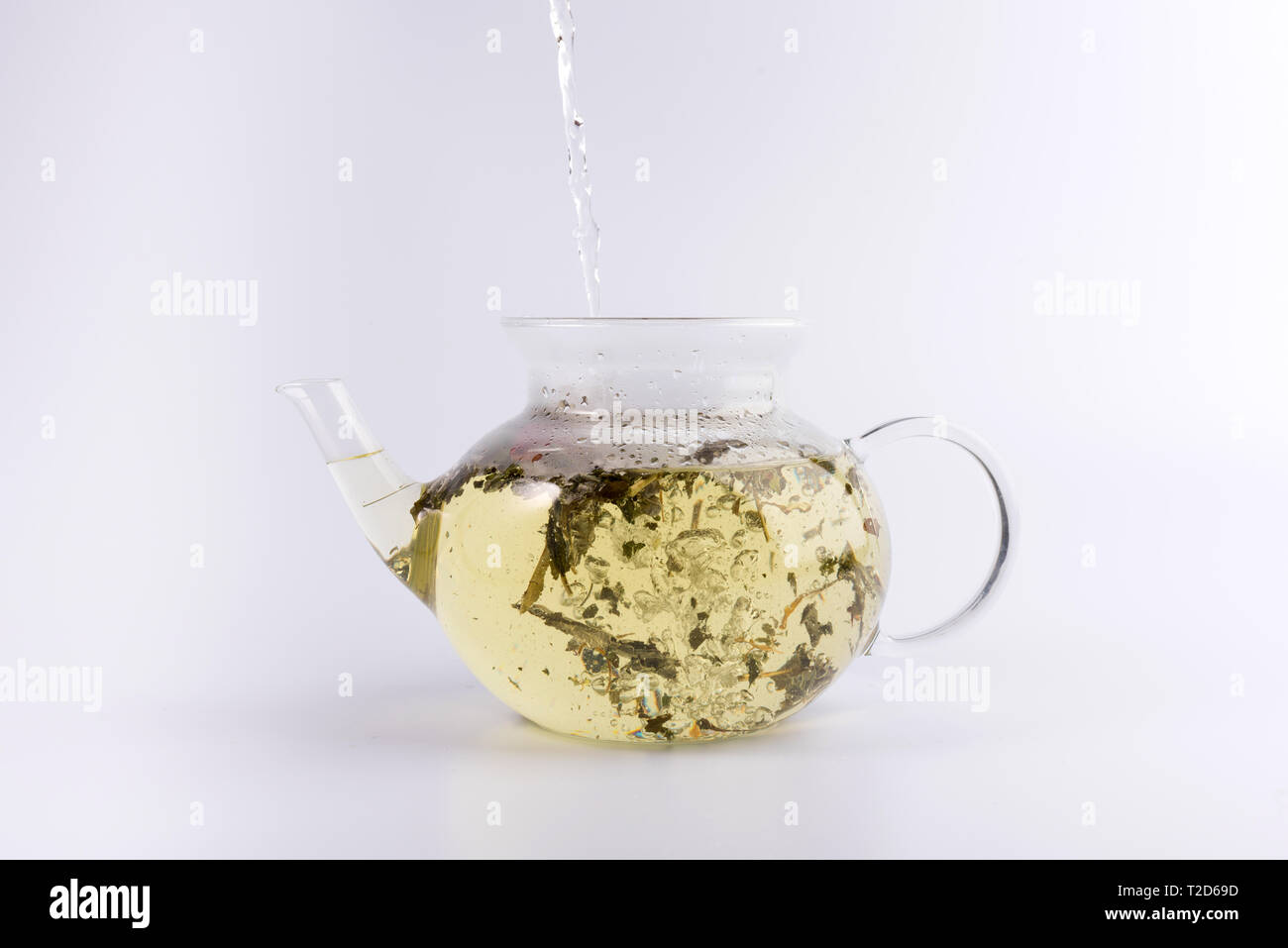 Pouring hot water to the glass teapot with herbal tea, isolated on white background Stock Photo