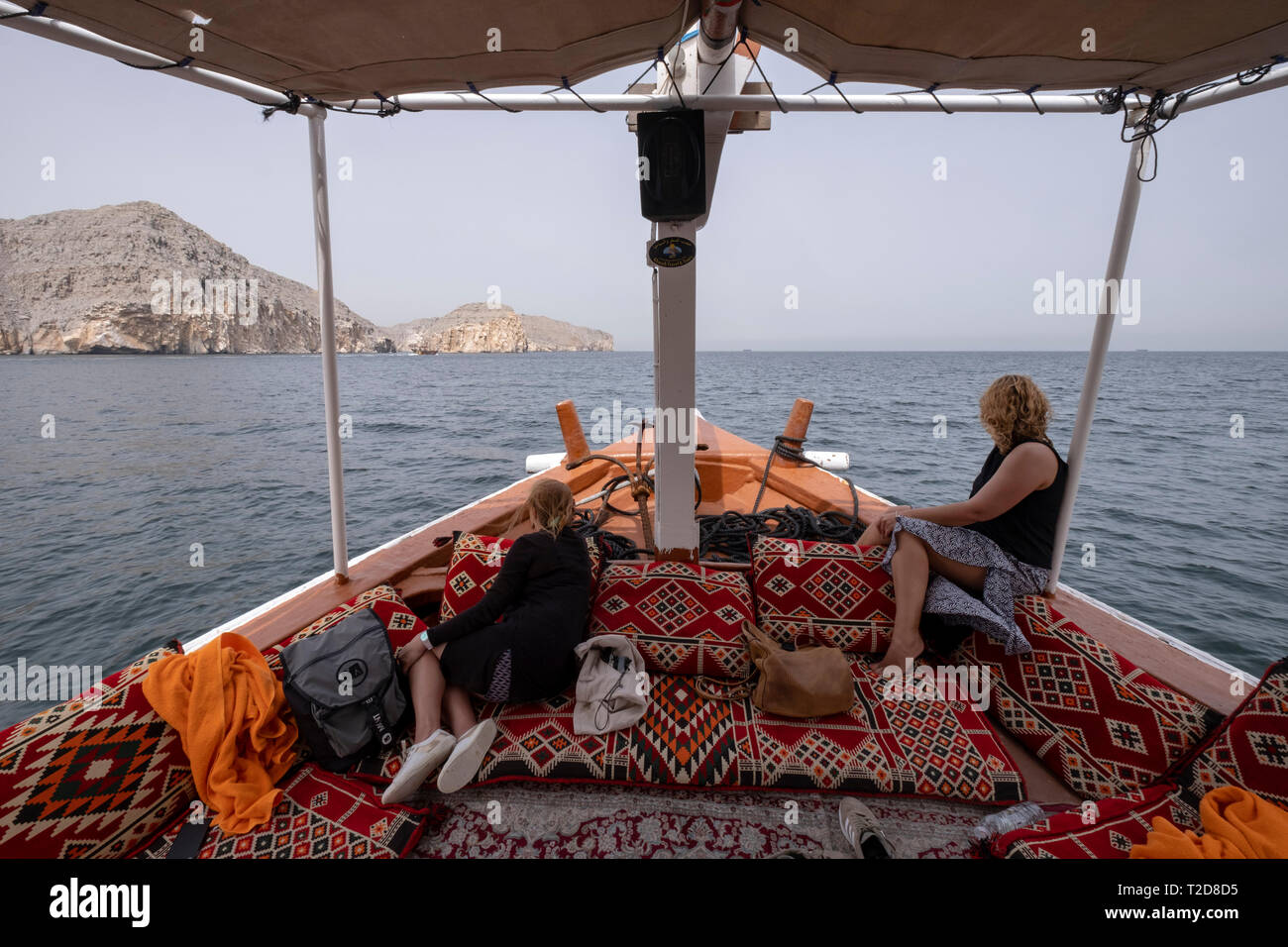Cruise tour aboard a traditionally decorated arabian Dhow wooden boat along the rocky mountains of the Musandam peninsula in the Oman Fjords Stock Photo