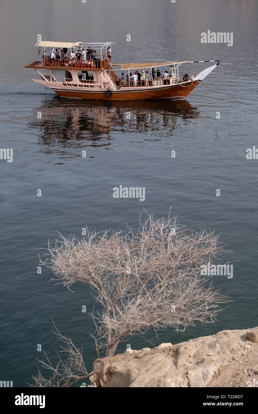 Traditionally decorated arabian Dhow wooden boat cruising along the rocky mountains of the Musandam peninsula in the Oman Fjords Stock Photo