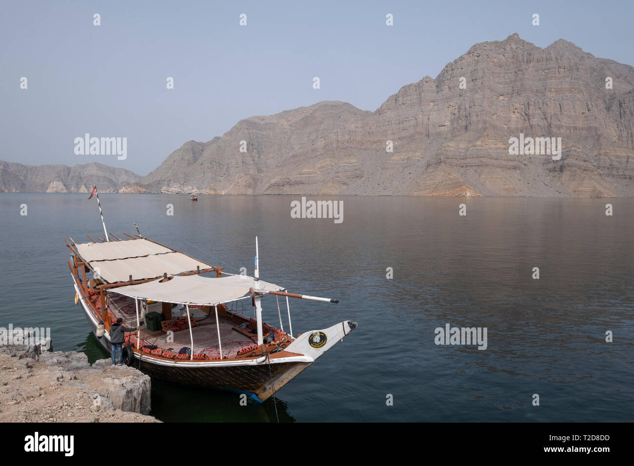 Traditionally decorated arabian Dhow wooden boat cruising along the rocky mountains of the Musandam peninsula in the Oman Fjords Stock Photo