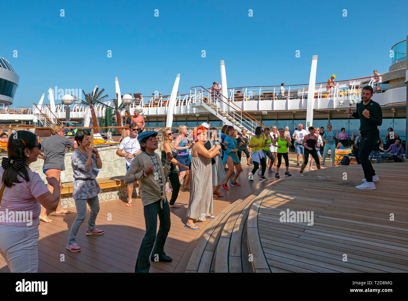 Passengers dancing on the deck of a cruise ship following the lead of a staff entertainer on stage during a dance class Stock Photo
