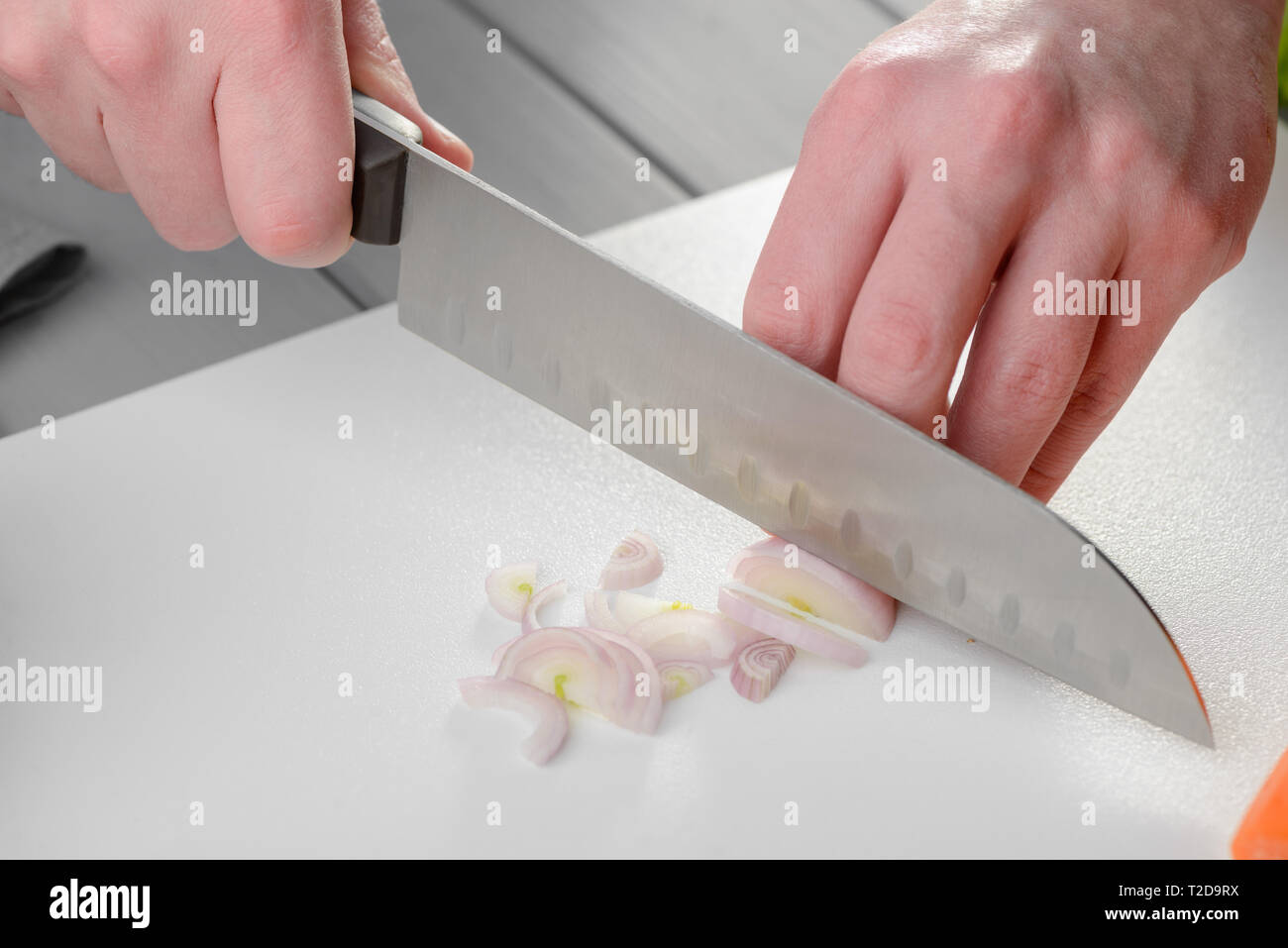 Man slicing an onion with a santoku knife. Cutting techniques, cooking