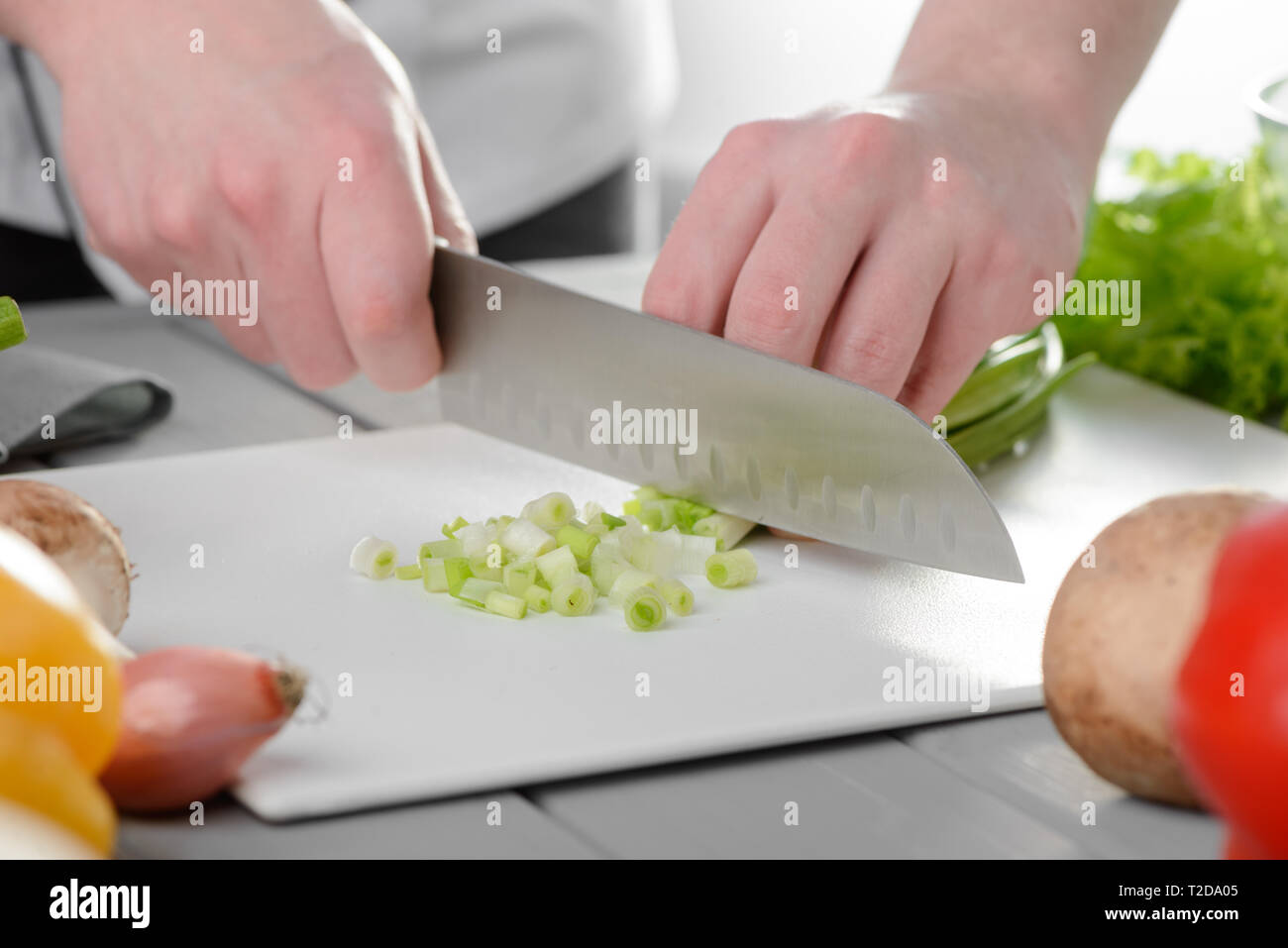 Chef chopping spring onions on a white board. Fast cutting and perfect ...