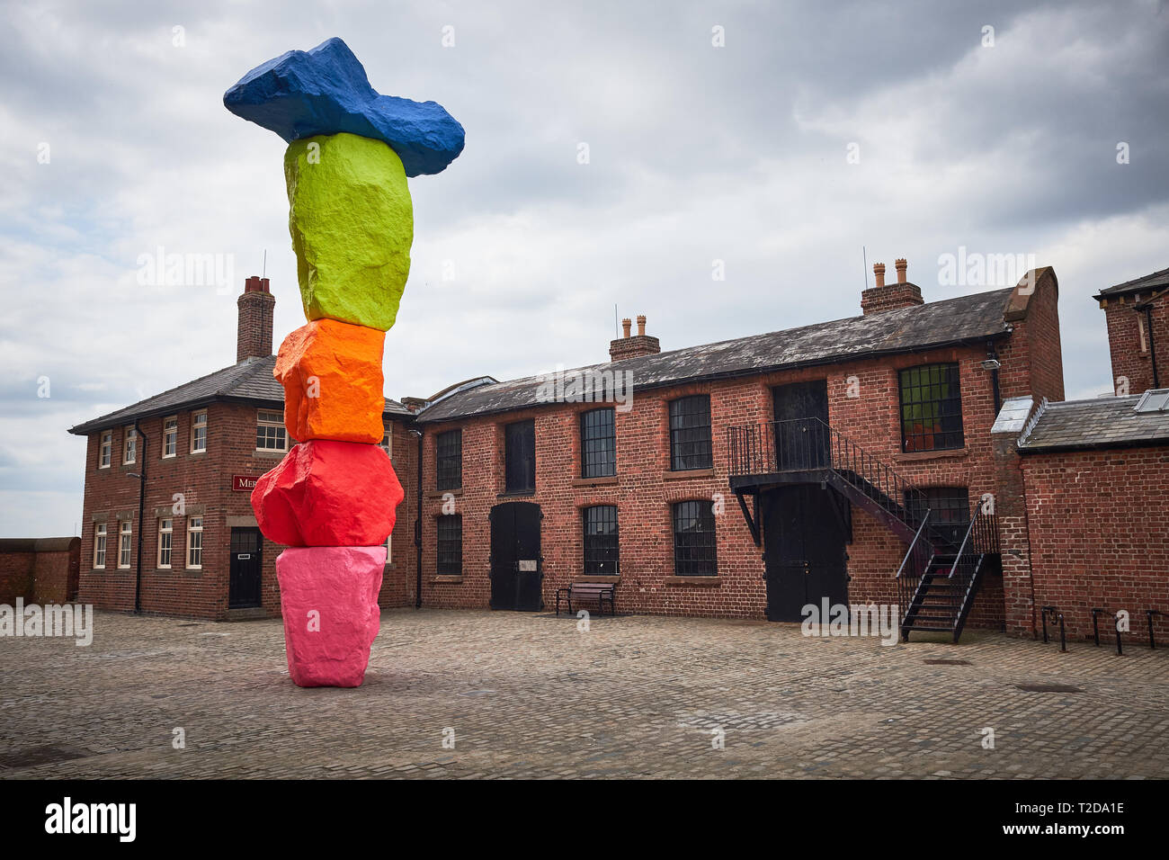 Outside the Tate Liverpool art gallery surrounded by buildings of the Royal Albert dock stands a sculpture by Ugo Rondinone named Liverpool Mountain Stock Photo