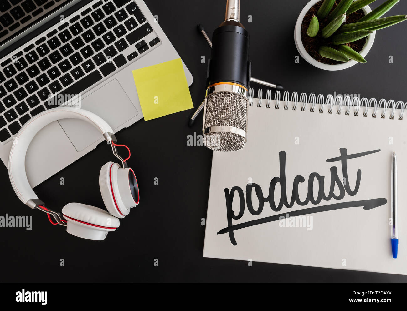 podcast recording concept with microphone, headphones and laptop computer next to note pad on dark table Stock Photo
