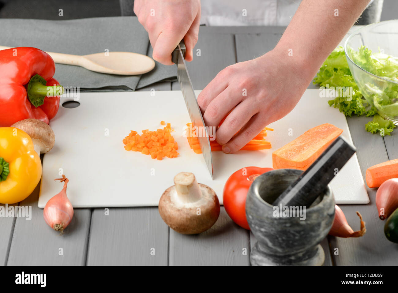 Man dicing carrot into small cubes on a white board. Cutting vegetables