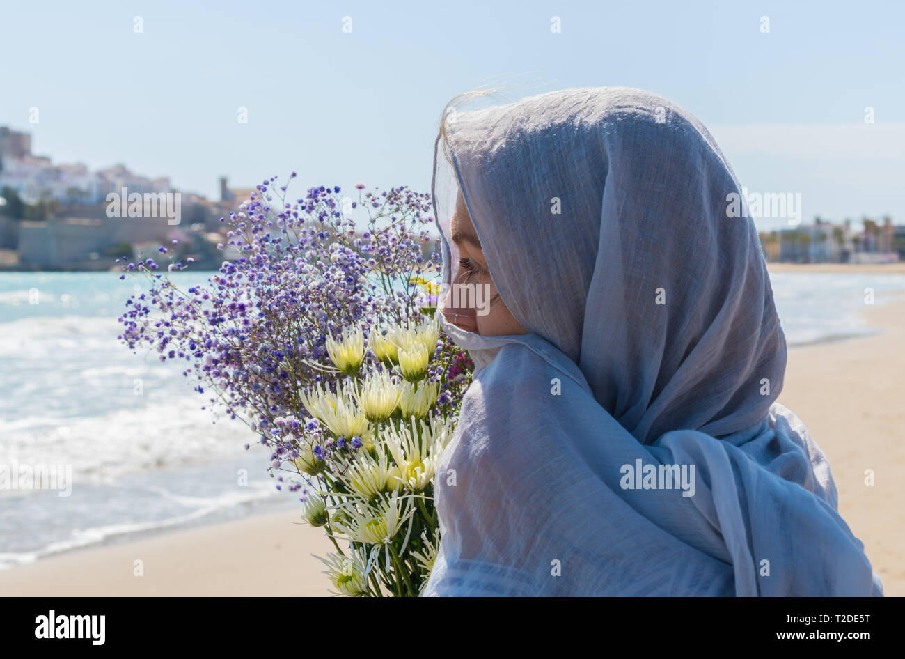 young women with light gray scarf and a bouquet of various flowers on the beach . Travel and holidays. Freedom concept Stock Photo