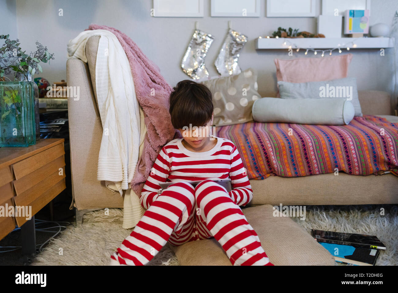 Boy in pajamas sitting on the family room with a tablet Stock Photo
