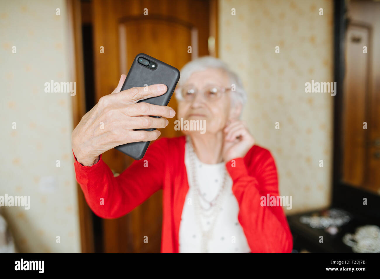 Well dressed gray haired fancy senior woman is making selfie in her bedroom. Stock Photo