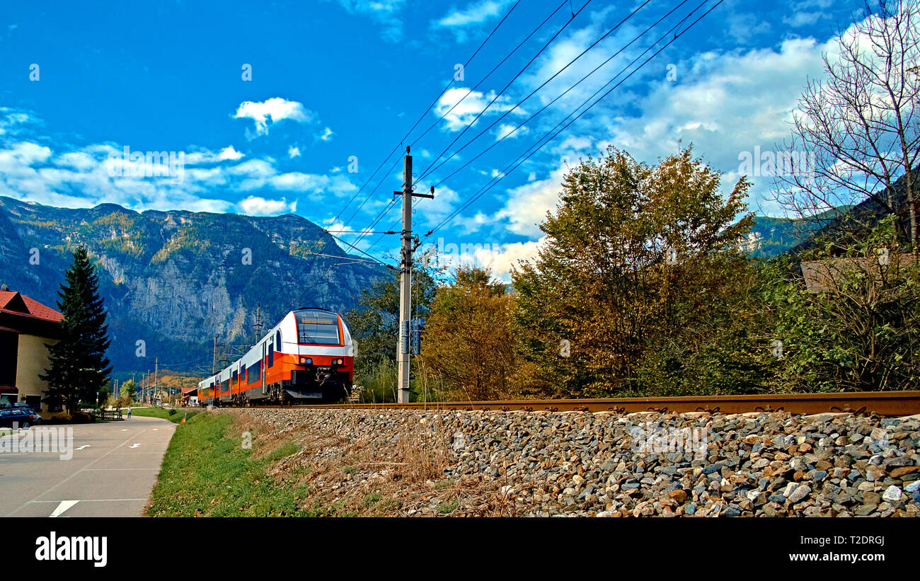 Red blue train in motion in Austrian alps mountains. High speed mountain train arrives at Hallstatt Obertraun train station in mountains. Location: re Stock Photo