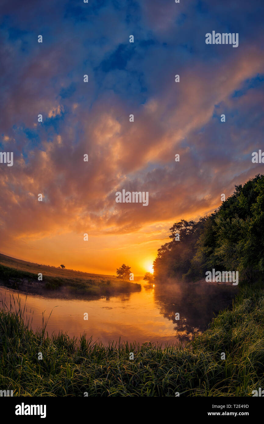 Beautiful morning on a river meander in a natural landscape with lot of fog and steam at sunrise and dramatic clouds against a blue sky shot with fish Stock Photo