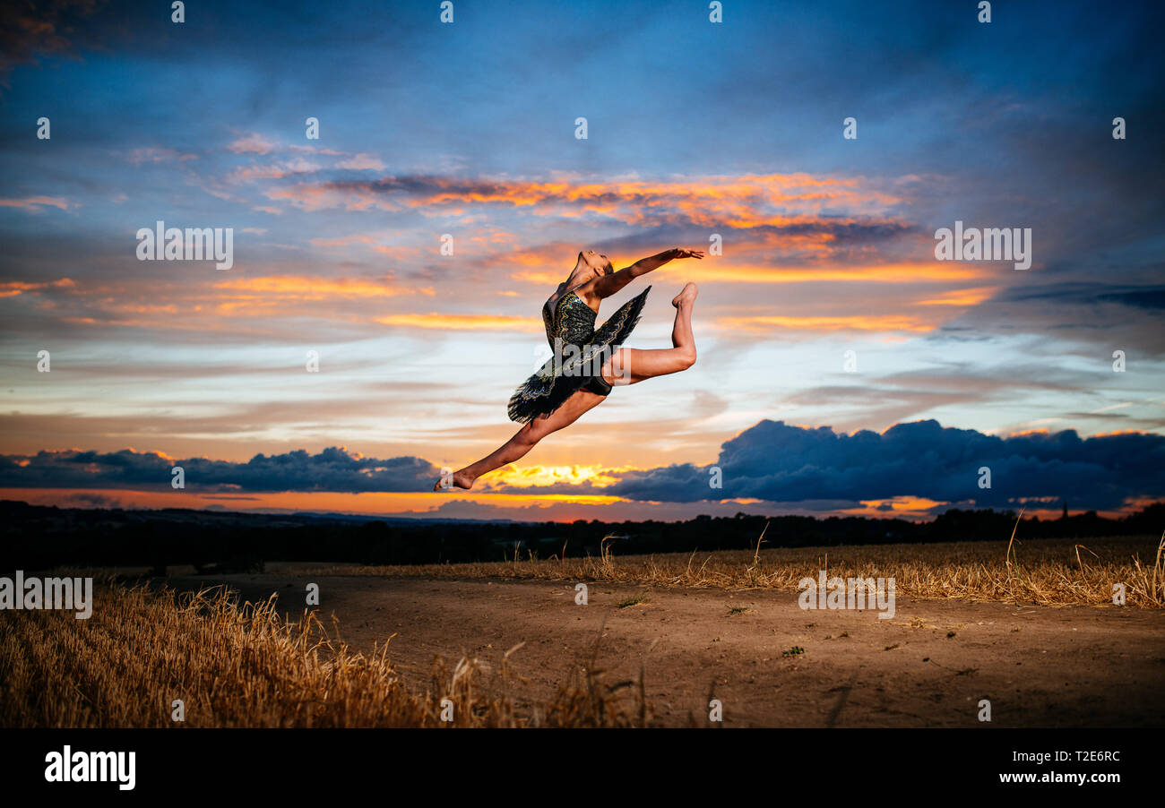 Ballet dancer leaping through air against beautiful sunset Stock Photo