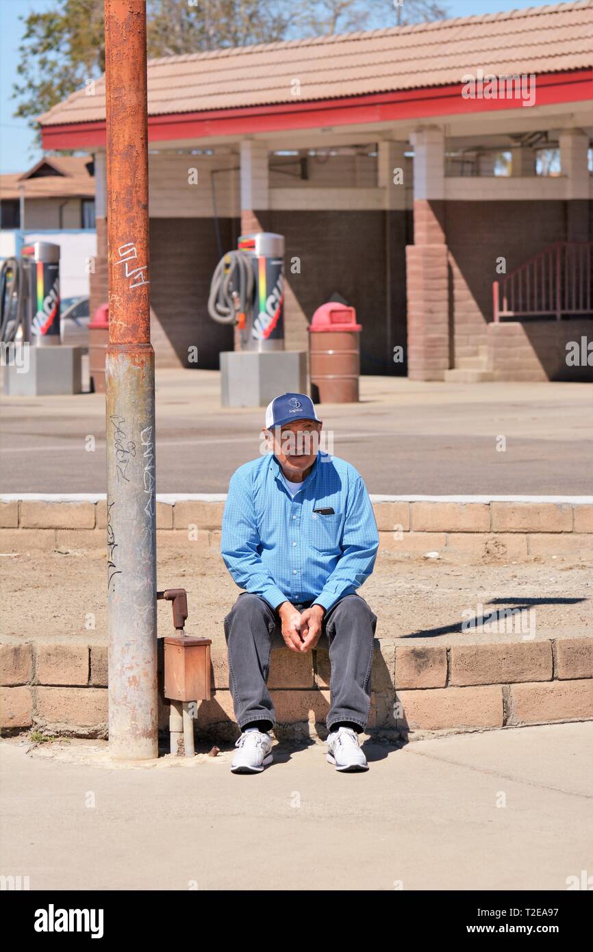 Senior Mexican ethnic man wanting day labor, 71 yo, sitting on street corner wanting work to help support himself in hard times - any labor work paid Stock Photo