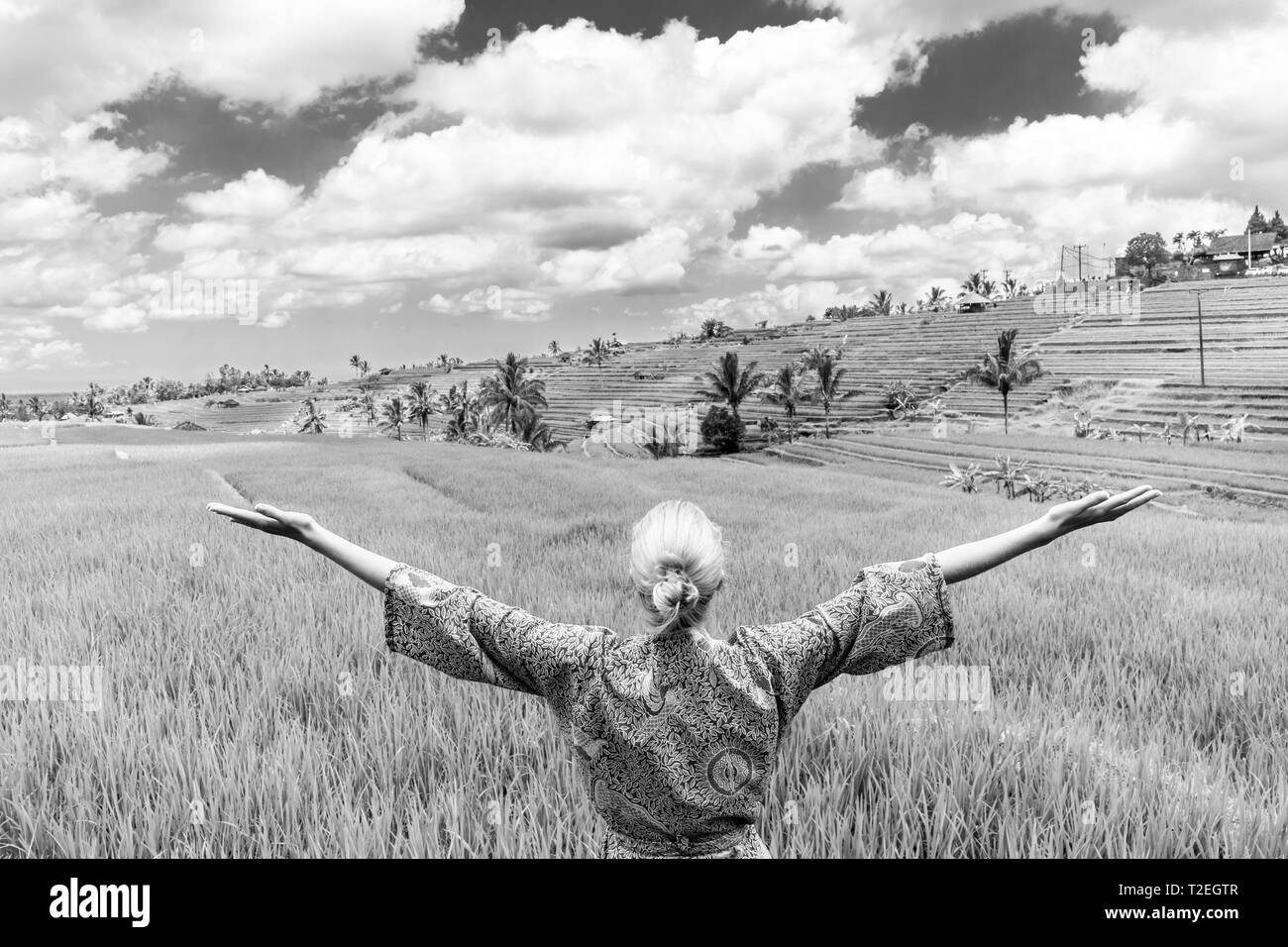 Relaxed fashionable caucasian woman wearing asian style kimono, arms rised to sky, enjoying pure nature at beautiful green rice fields on Bali island. Stock Photo