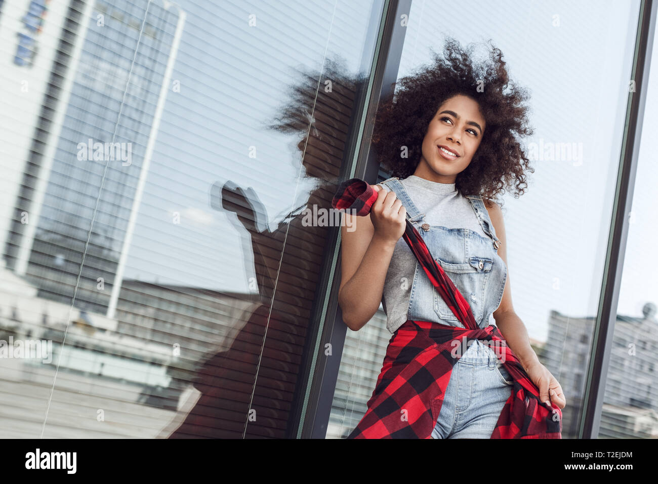 Young woman in the city street standing leaning on window looking aside smiling dreamful holding jacket sleeves Stock Photo