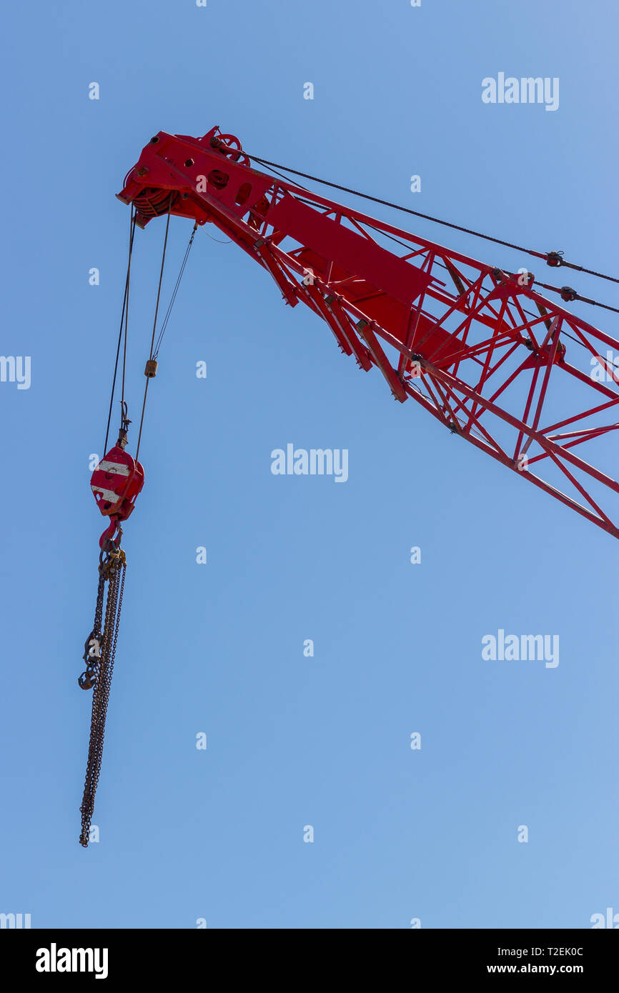 Red crane top with hook and lifting chains against clear blue sky Stock Photo