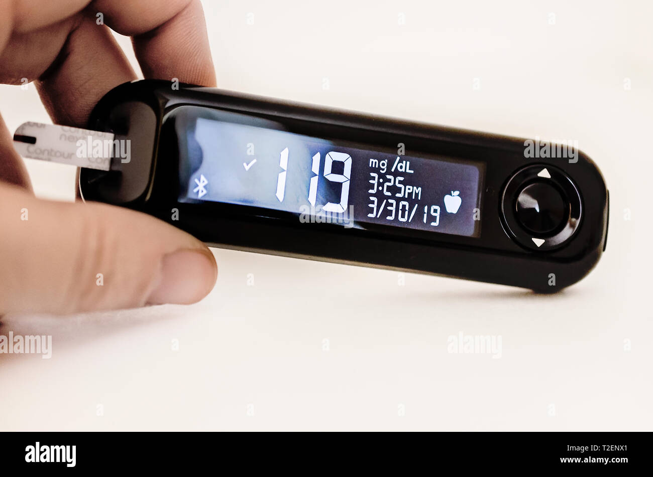 A hand holds a Contour Next blood glucose meter indicating a high blood sugar reading of 119 before a meal. Stock Photo